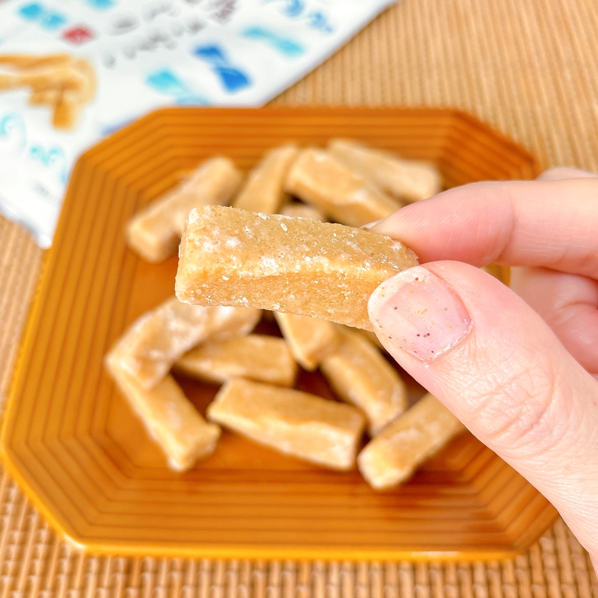 手に持たれたビスケット状のスナックがオレンジの皿に盛られている。