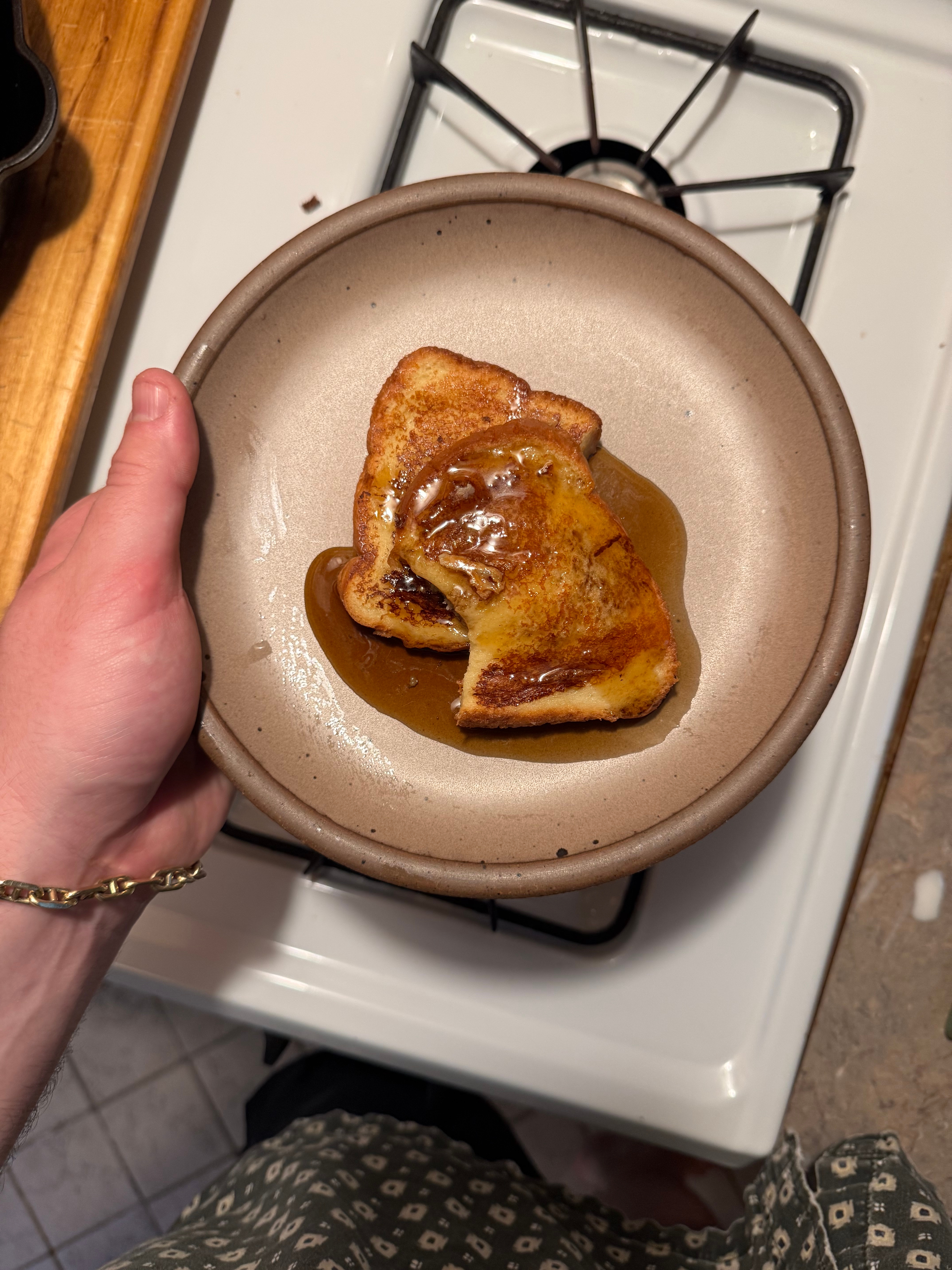 Person holds a plate with French toast drizzled in syrup over a stove