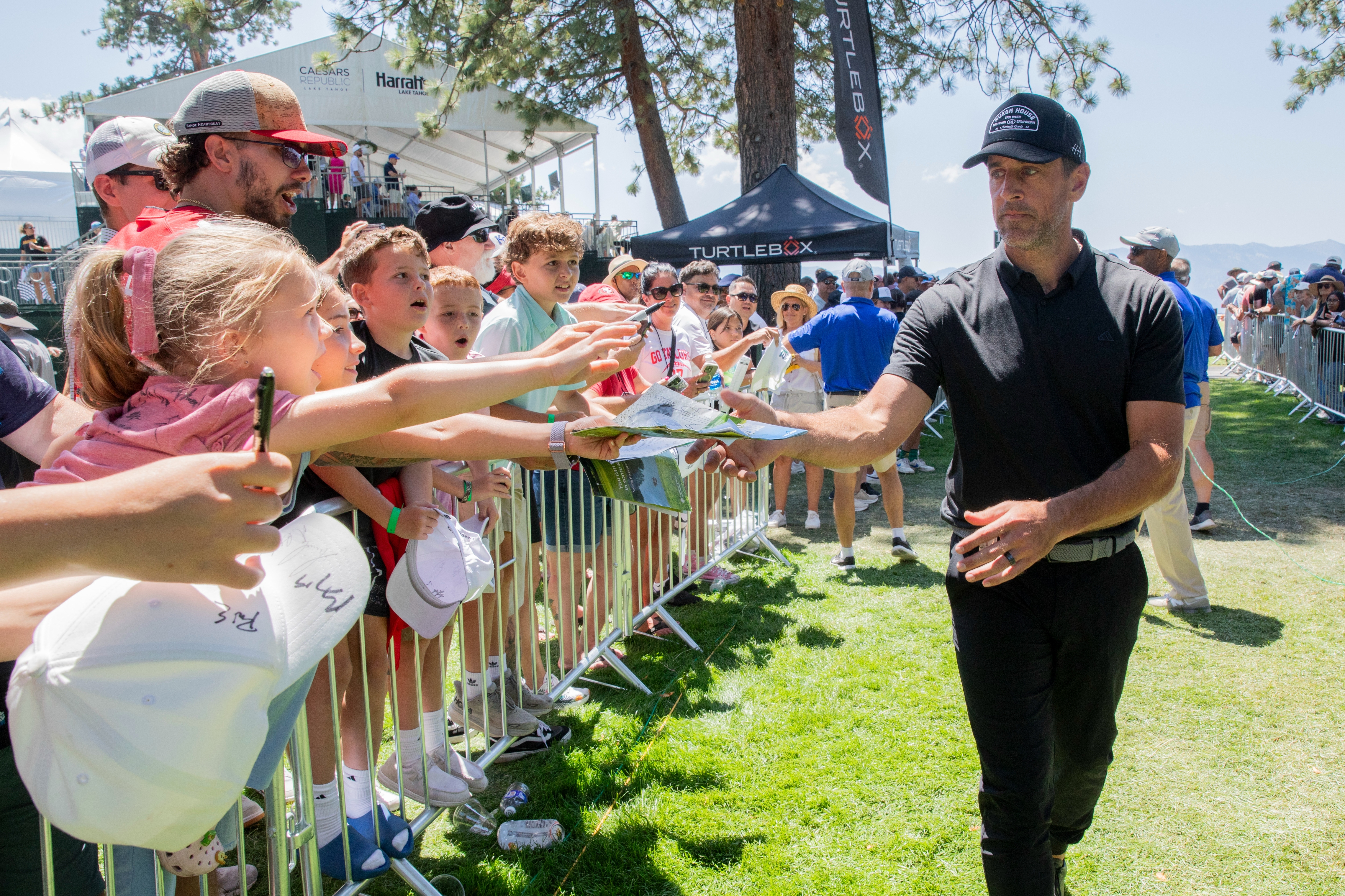 A celebrity in casual attire signs autographs for enthusiastic fans near a sports field