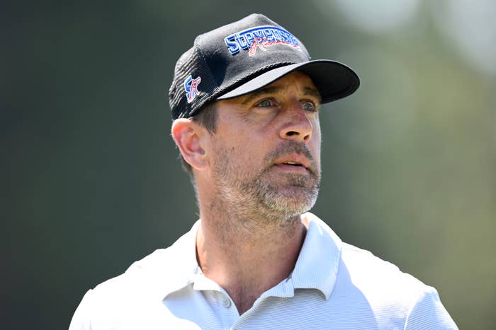 A person wearing a cap with embroidered text, outdoors in natural lighting, looking away from the camera
