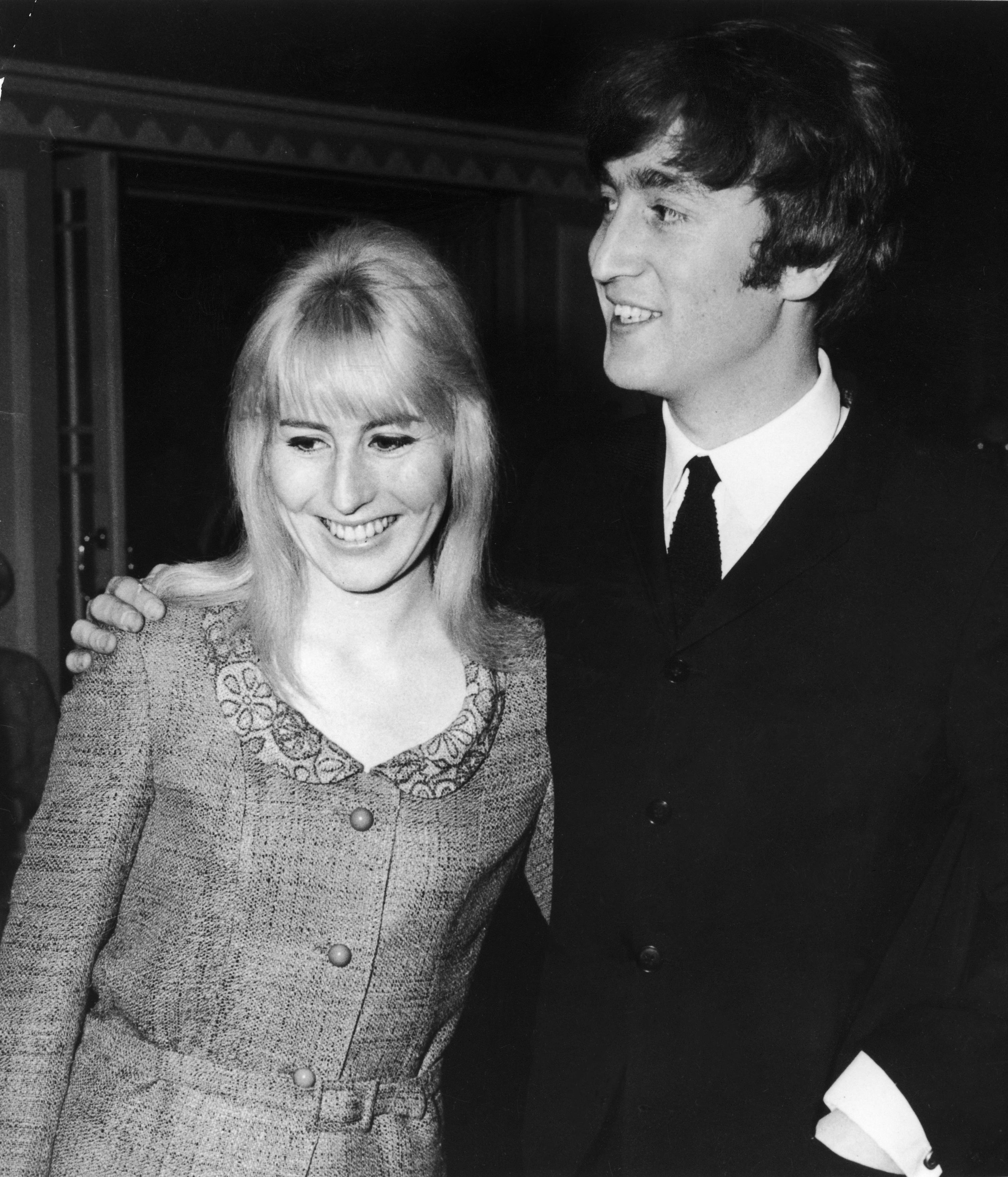 A man in a suit and tie smiles with a woman in a patterned long-sleeve dress. They are posing closely together