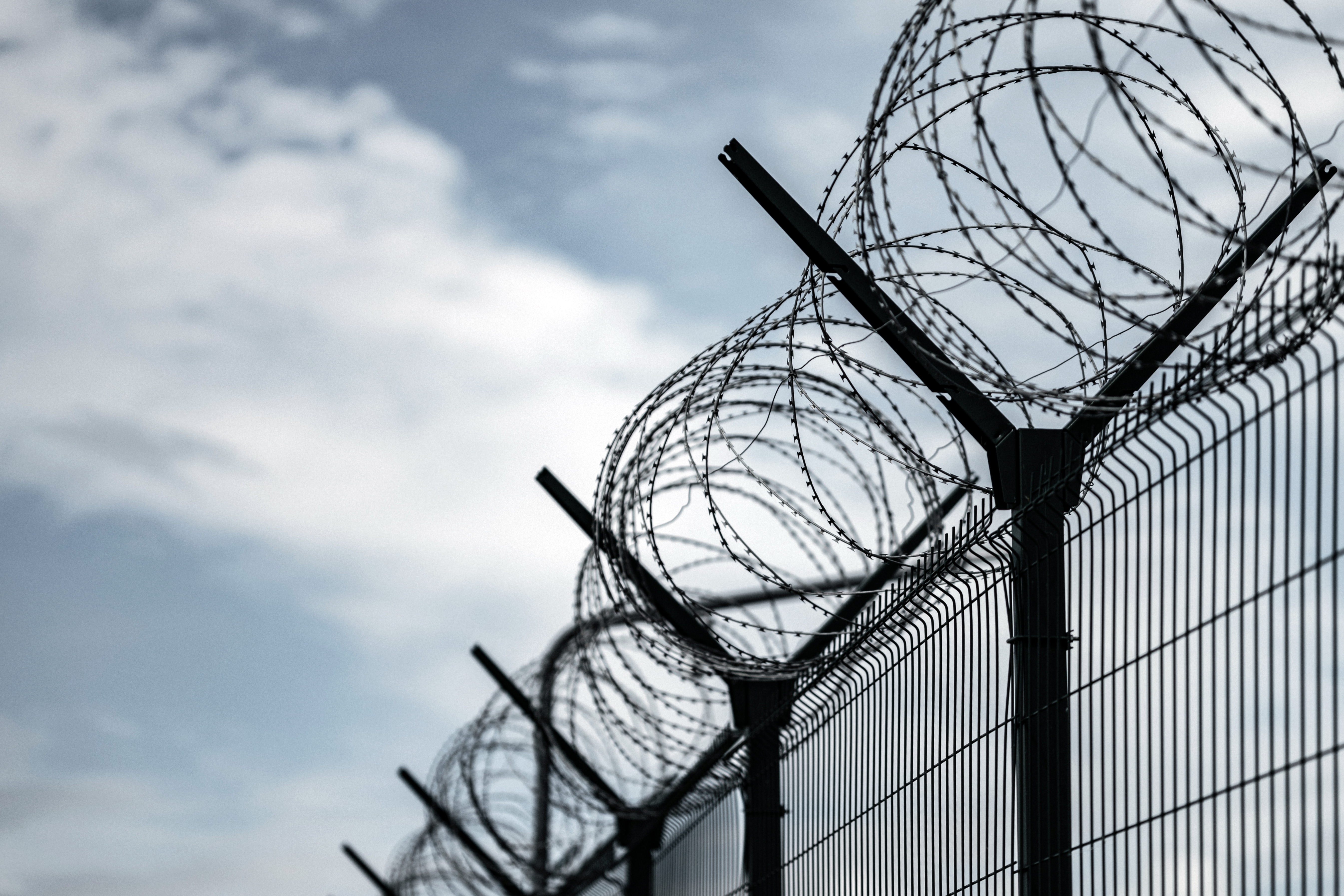 Barbed wire fence against a cloudy sky, suggesting a secure or restricted area