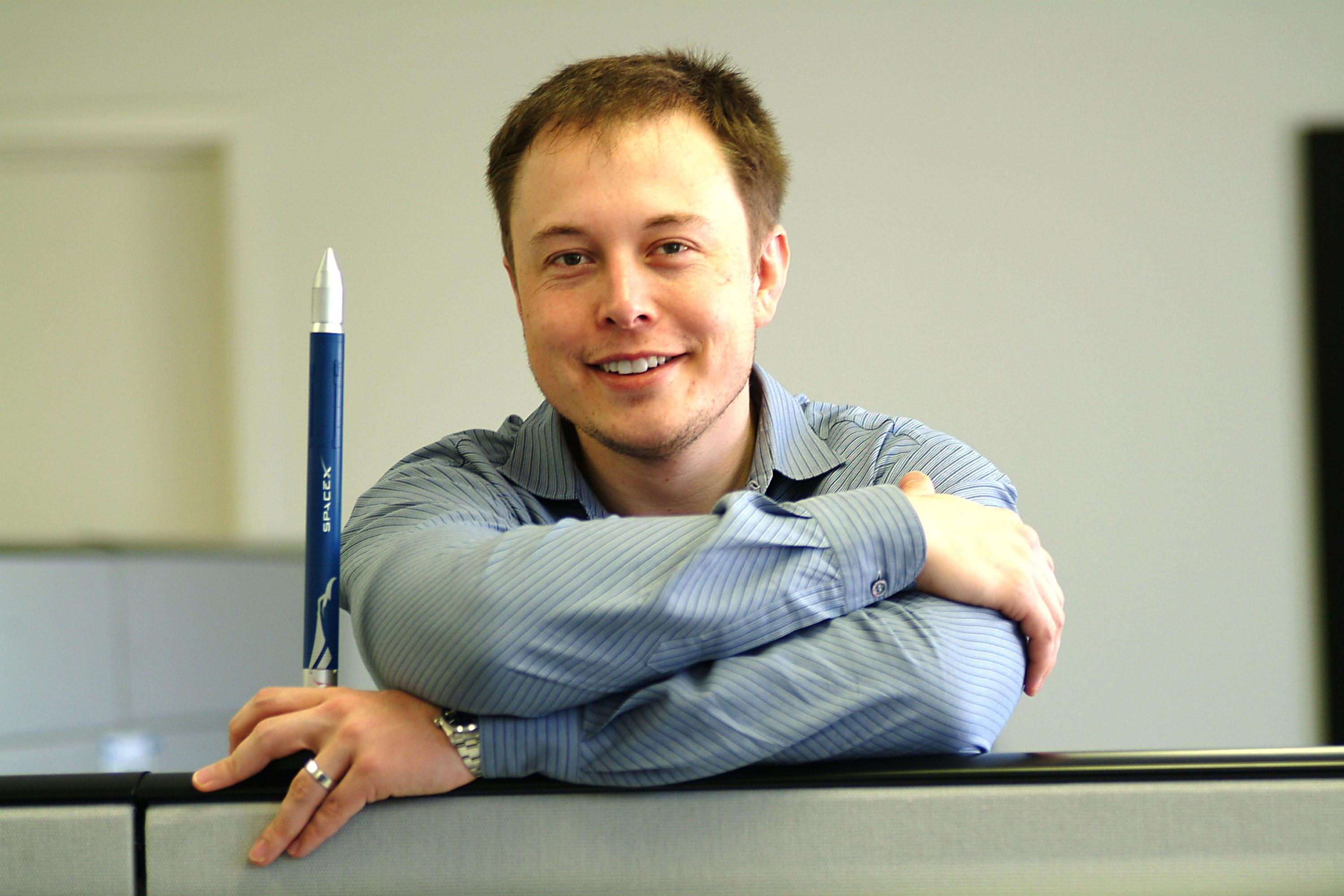 I don&#x27;t know who this person is. A person in a button-up shirt smiles, leaning on a partition with a pen-like object beside them