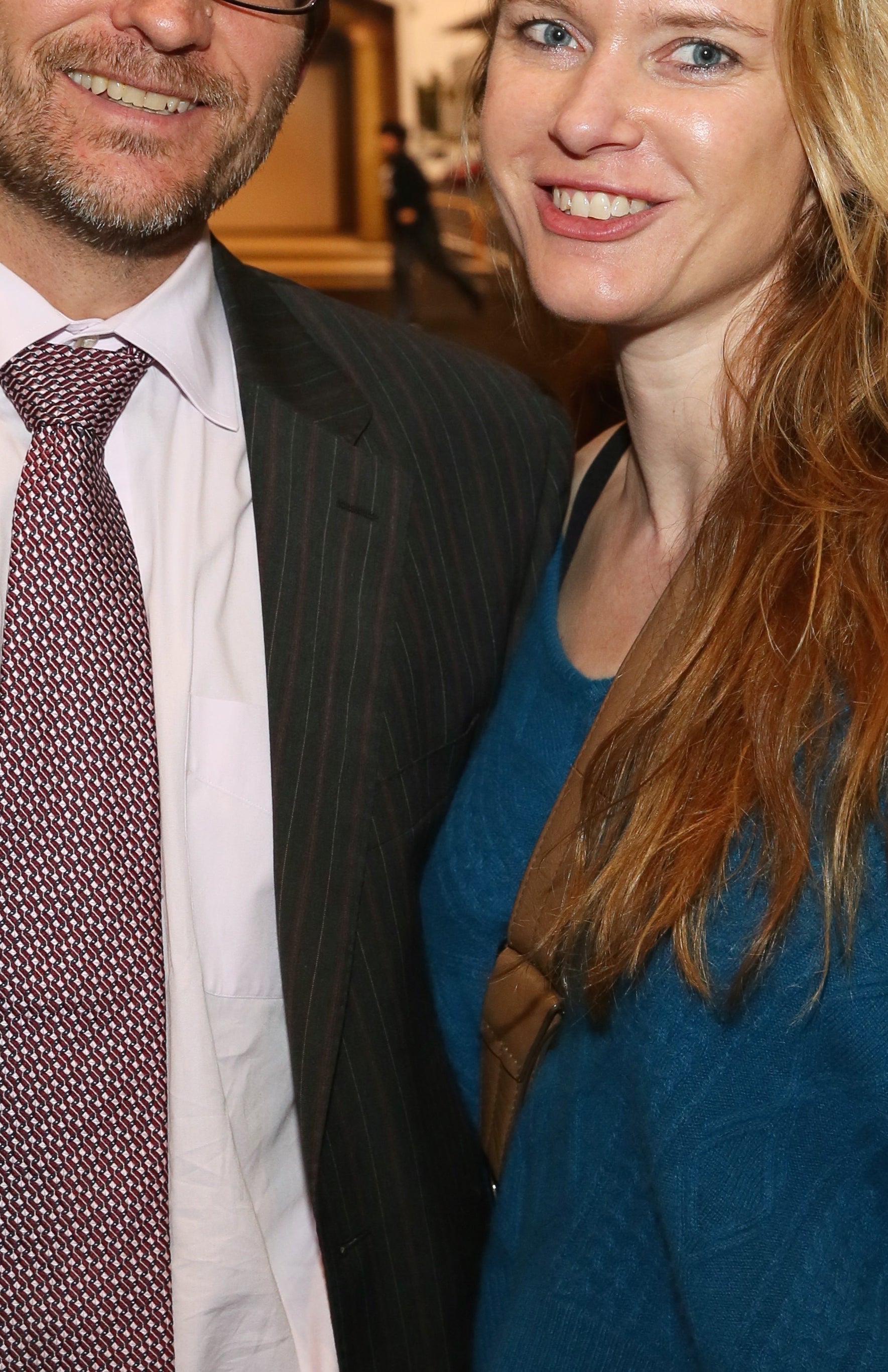 A man in a suit with a tie and a woman in a casual sweater smile for the camera at an indoor event