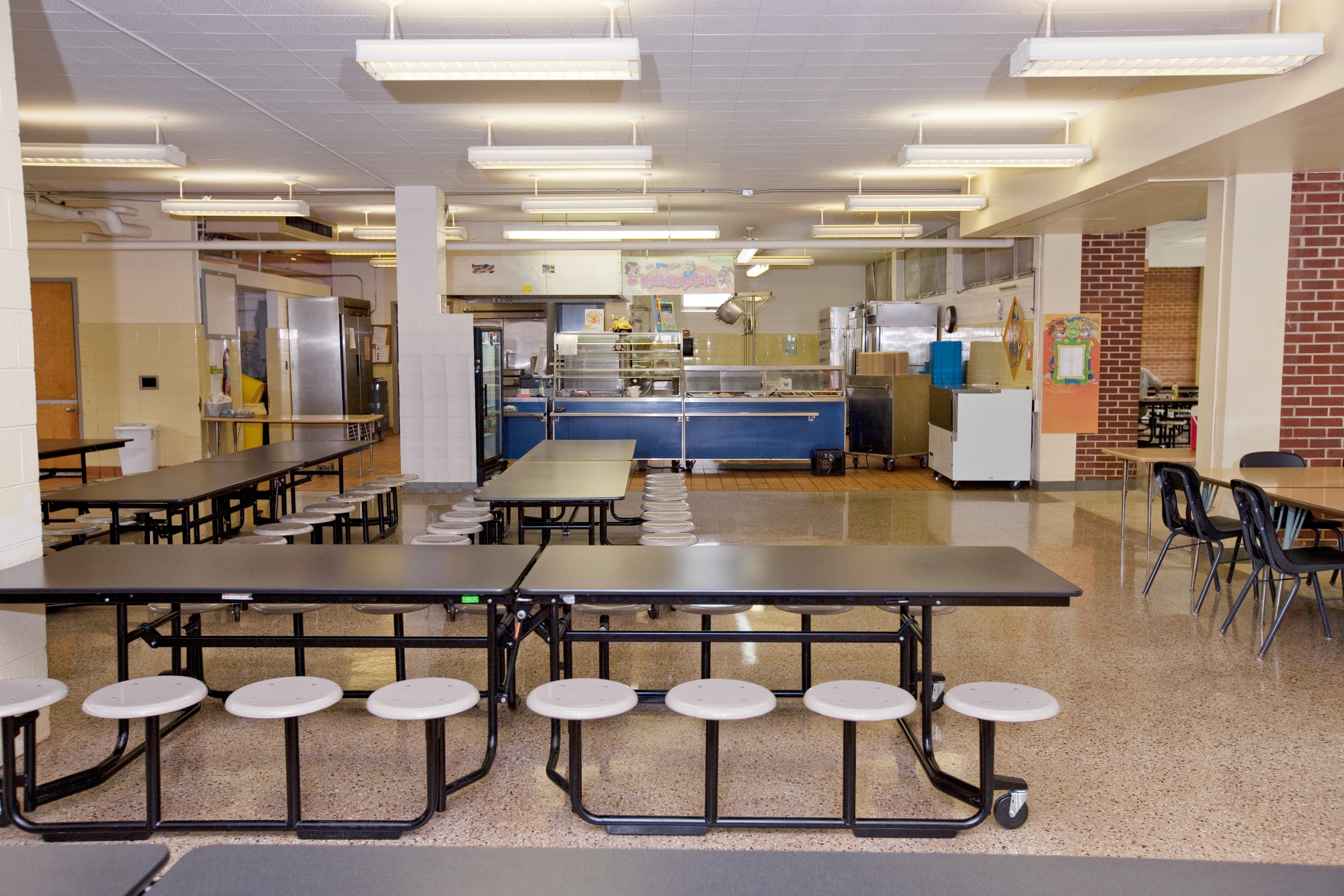 Empty school cafeteria with tables, chairs, and food service area in the background