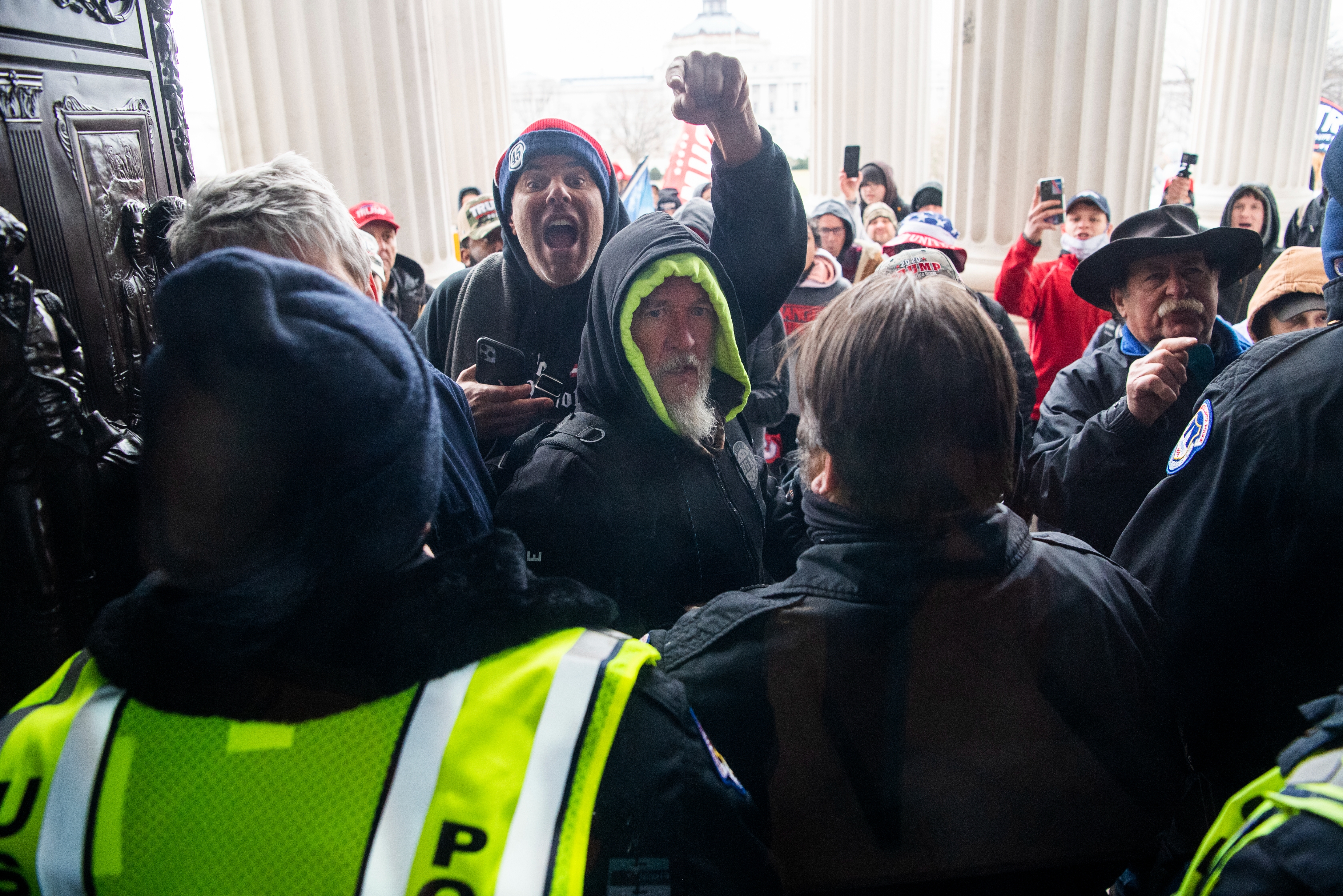 Crowd of people confronts police officers inside a building, with one person raising their fist