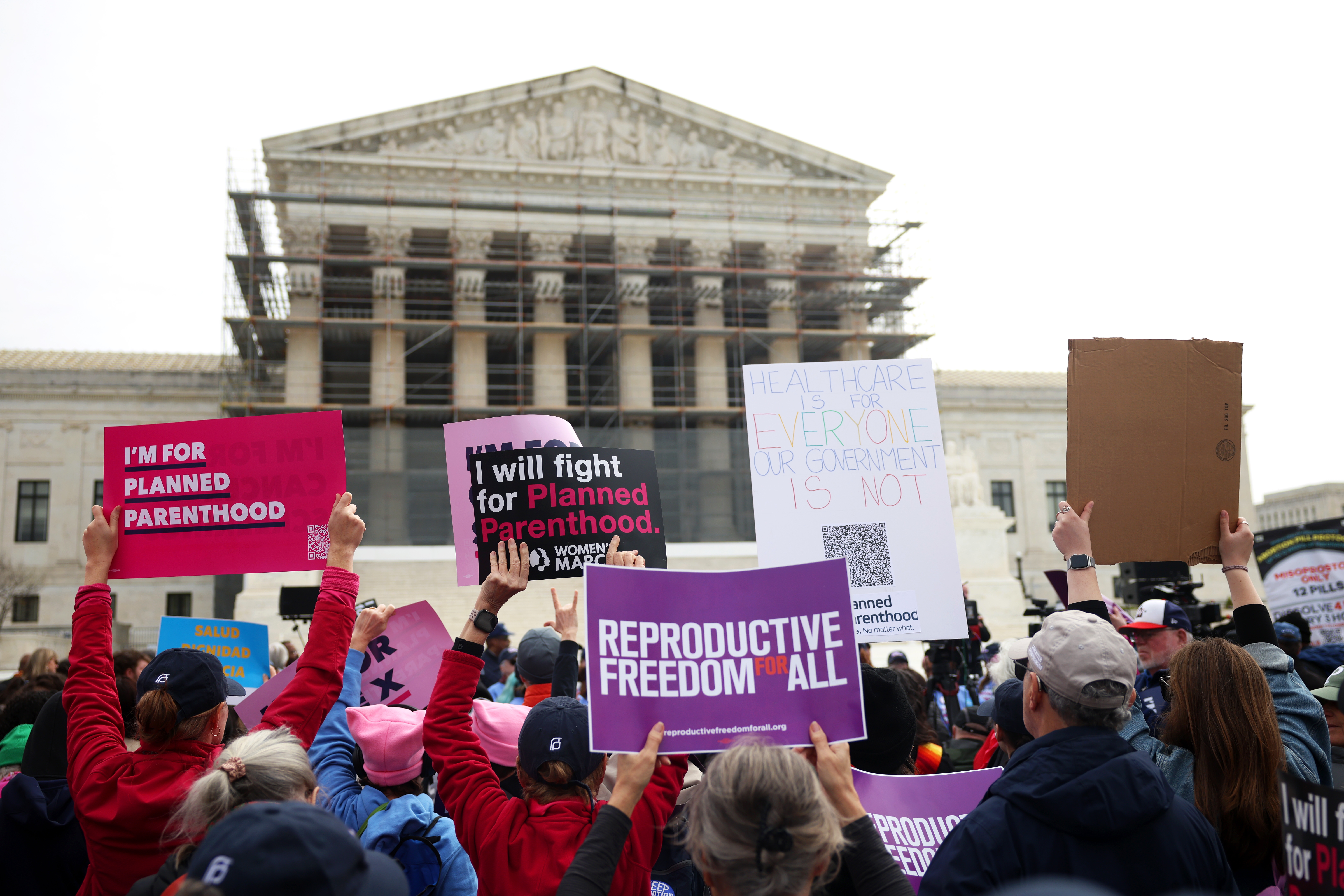 Protesters hold signs advocating for Planned Parenthood, reproductive rights, and against government interference outside a large government building