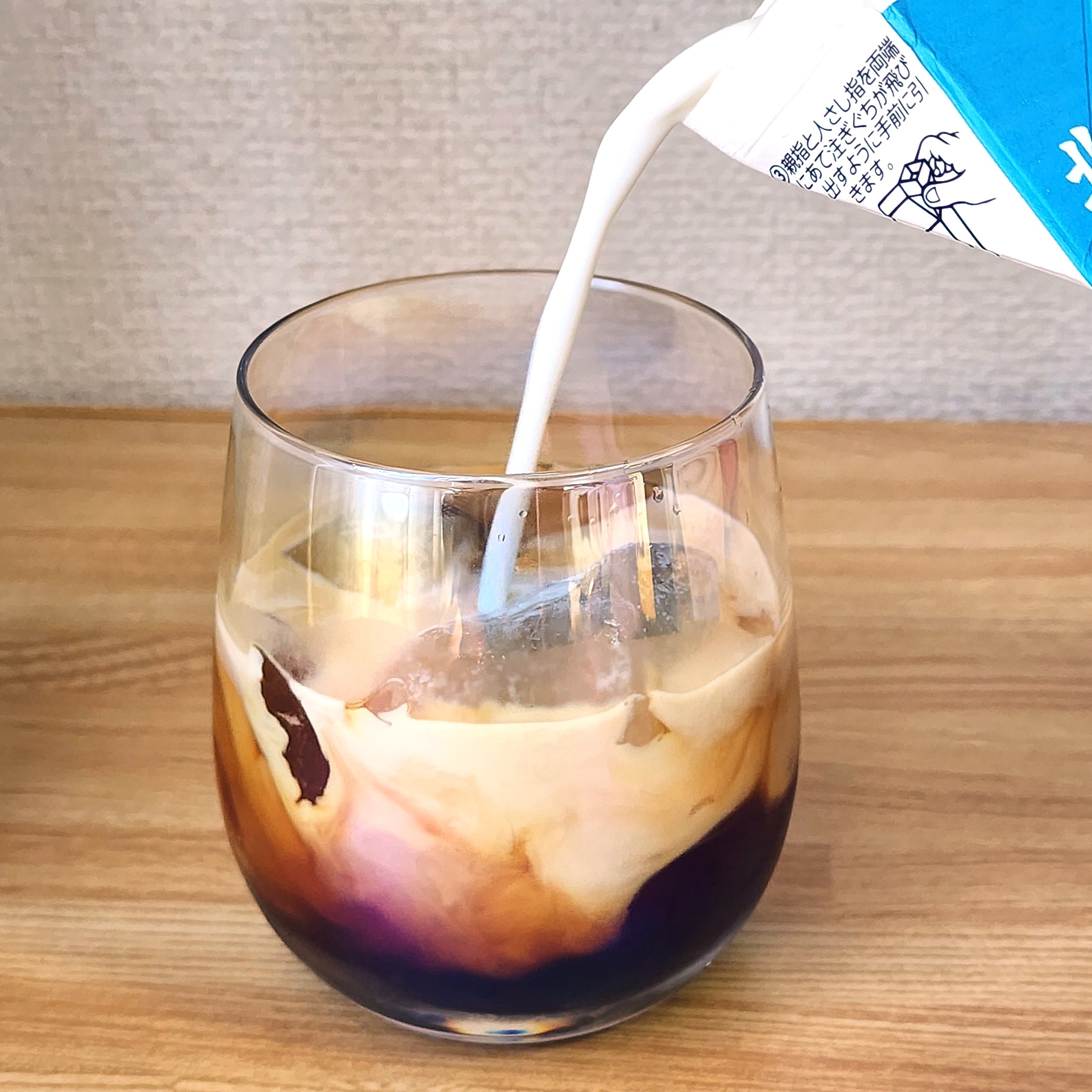 グラスに注がれるミルクがアイスコーヒーと混ざっている様子。