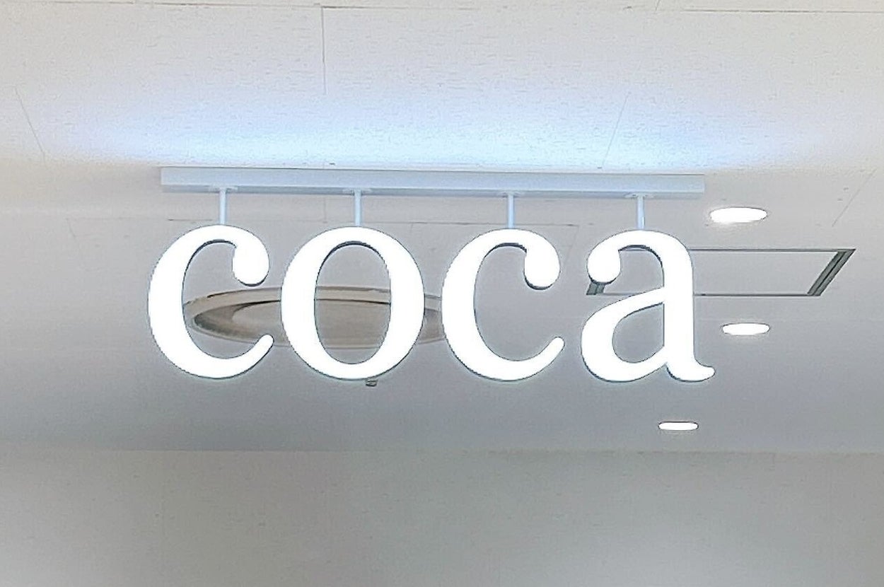 店内のネオンサインで「coca」と表示されています。背景には衣服が見えます。