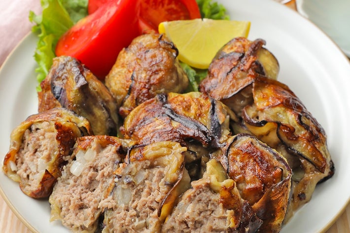 お皿に盛られたナス巻きの肉料理。付け合わせにトマト、レタス、レモンが添えられている。