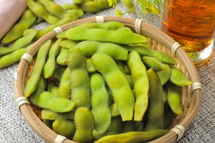 竹のざるに盛られた枝豆と横に置かれた冷たい飲み物。リネン素材のナプキンが横に見える。