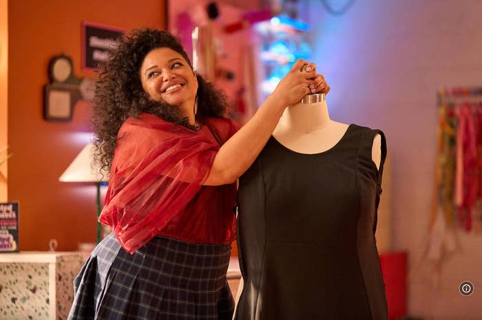 Person smiling, posing with a mannequin dressed in a sleeveless black dress, in a lively room setting