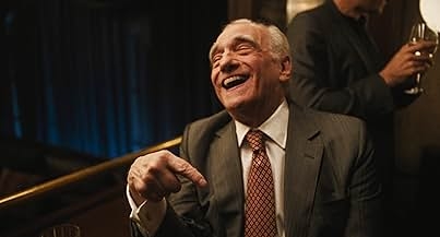 Elderly man in a suit, laughing and pointing at something off-camera, in a social gathering setting