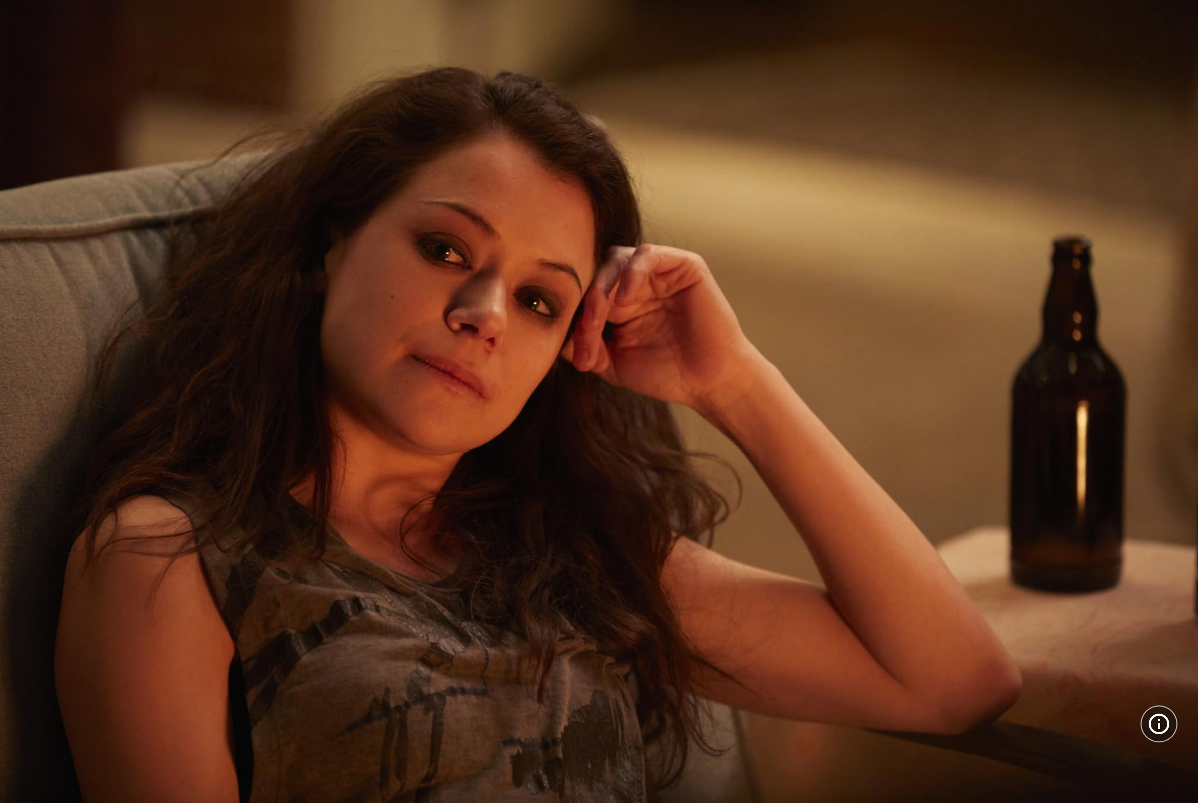 Person relaxing on a couch with a contemplative expression, hand resting on their chin, and an unlabelled bottle on a table nearby