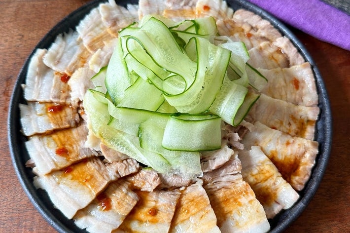 お皿に盛られた薄切りの肉ときゅうりの添え物。背景に箸と紫色の布。