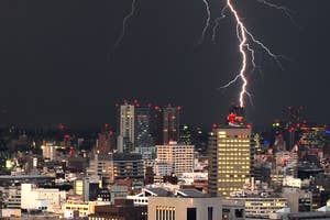 都市上空に雷が落ちる夜景。建物が立ち並ぶ中、稲妻が一際目立つ。