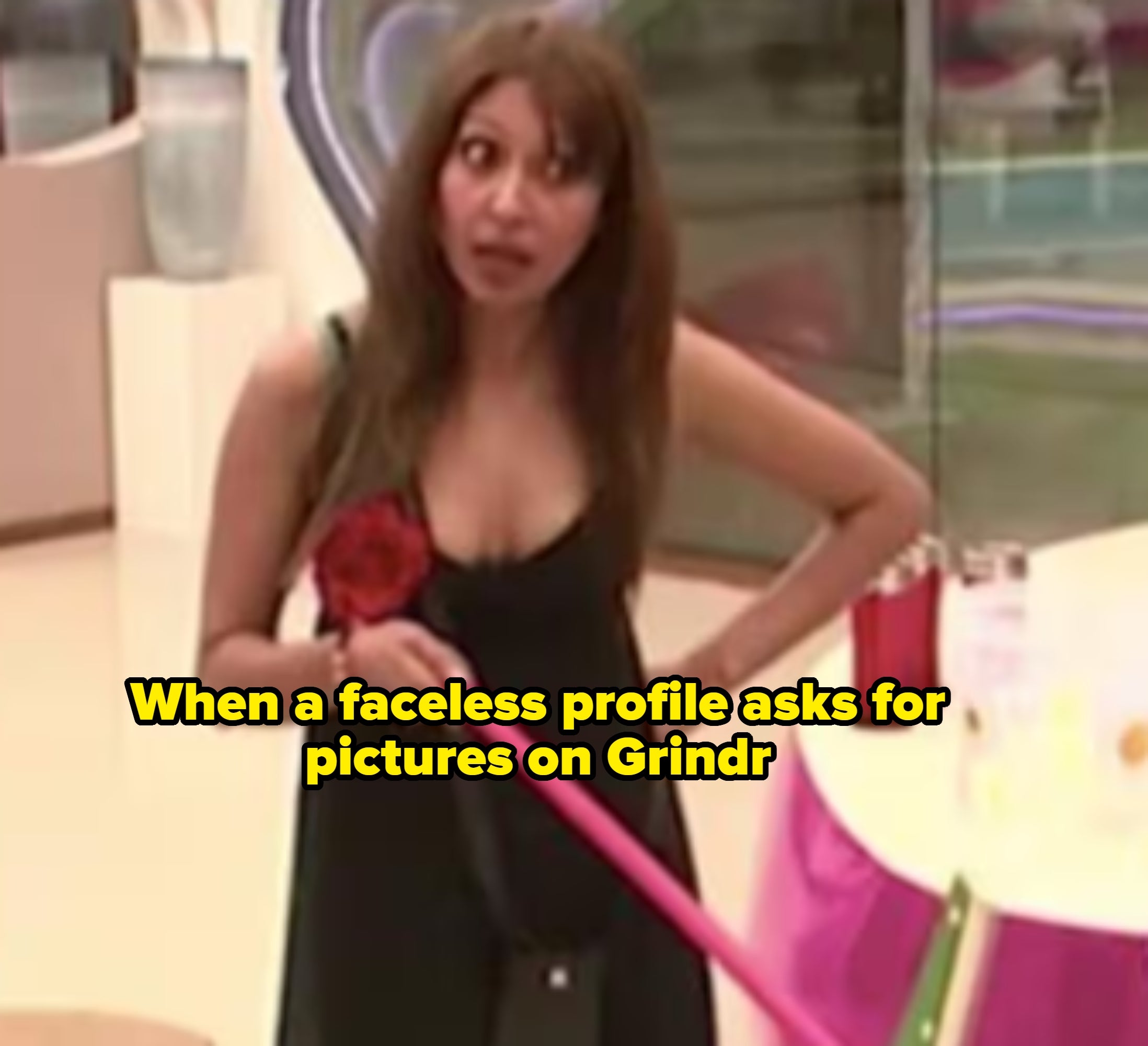 Person in sleeveless dress, holding a broom, standing indoors with a surprised expression