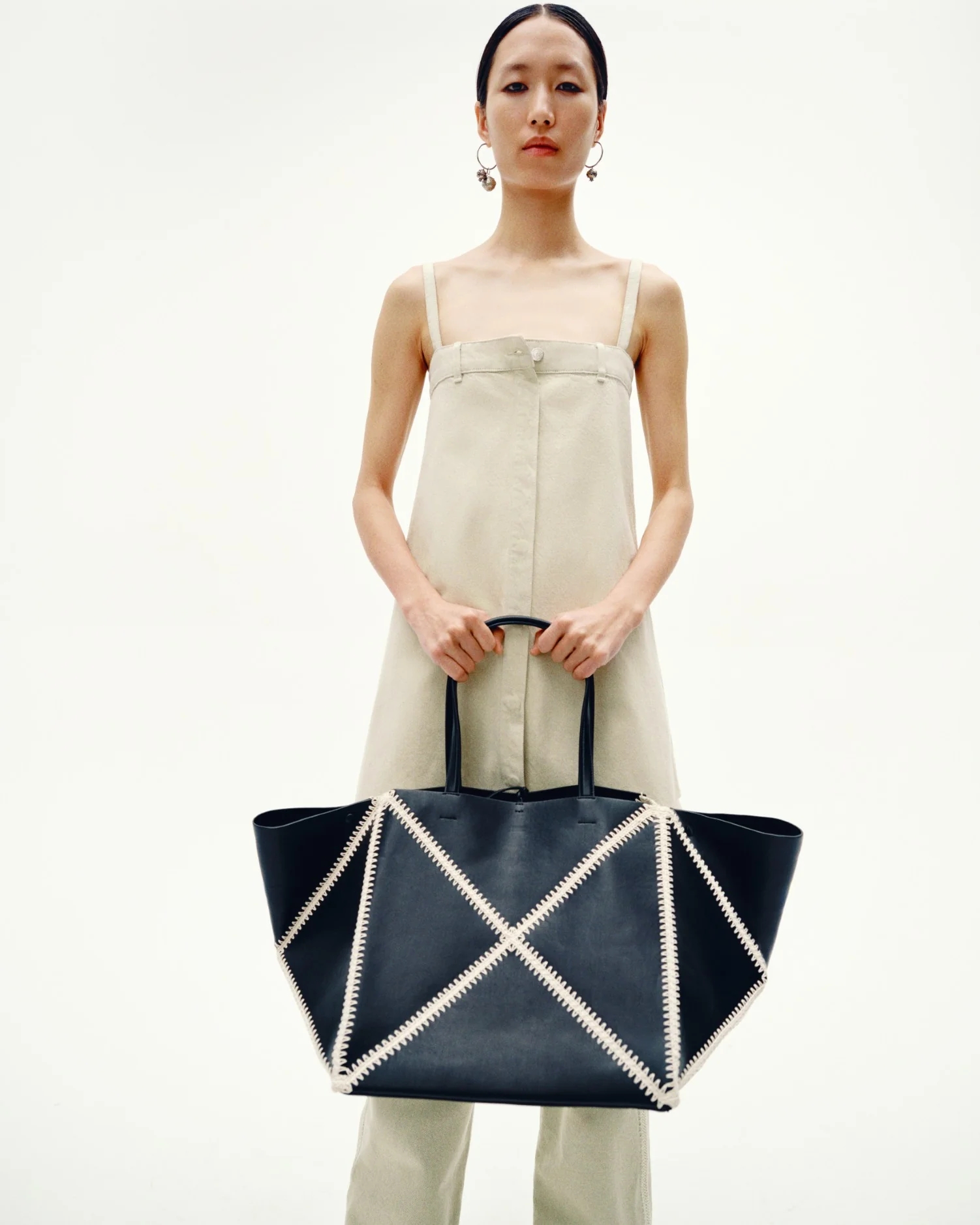 Person in a sleeveless dress holding a large geometric-patterned tote bag, posing against a plain background