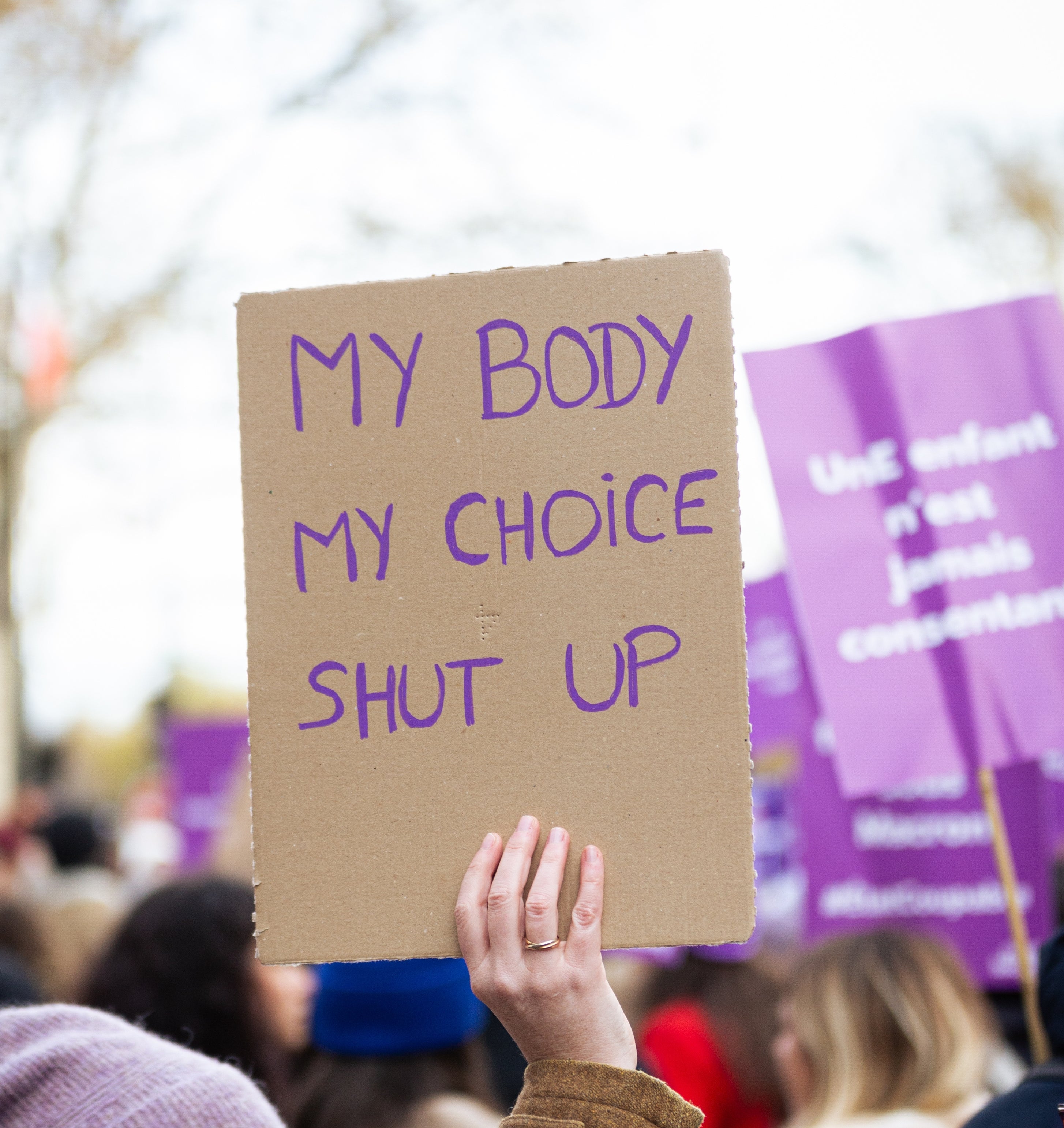Personen som holder et tegn som leser & quot; My Body My Choice Shut Up & Quot; ved en protest. Andre demonstranter og tegn er synlige i bakgrunnen