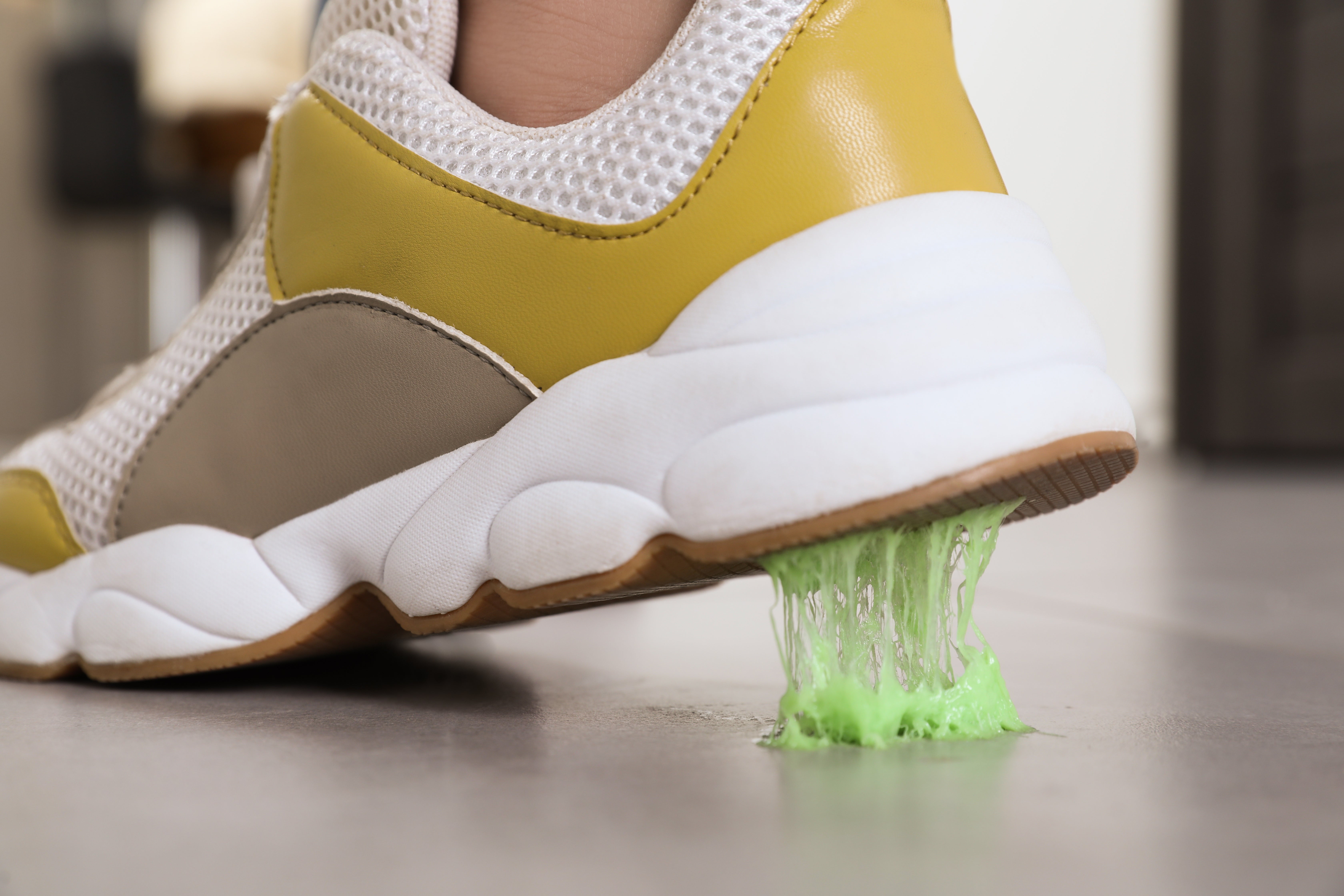 Sneaker menginjak permen karet hijau terang di trotoar, pemandangan sol sepatu dari dekat