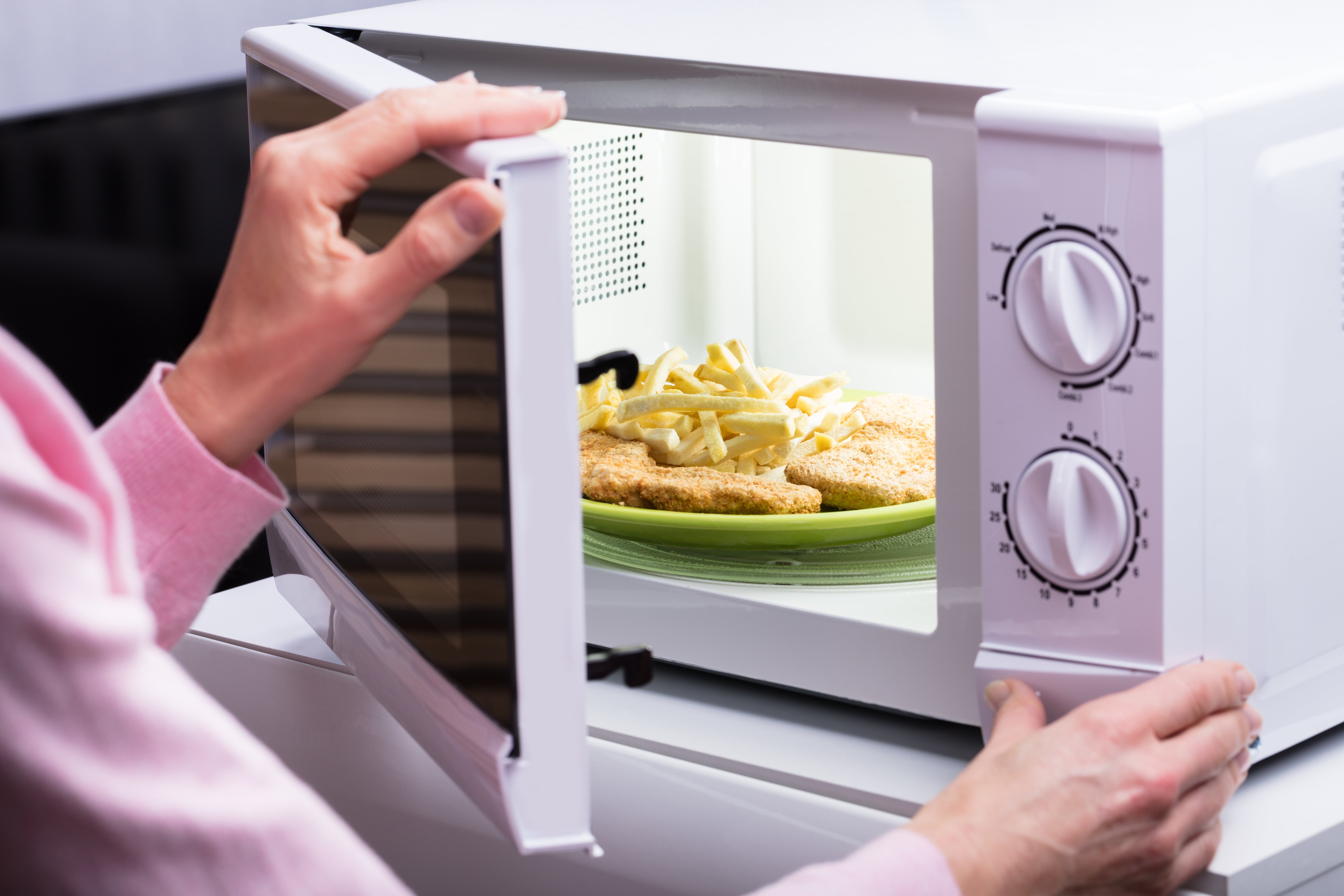 Orang menempatkan piring dengan roti ayam dan kentang goreng ke dalam microwave