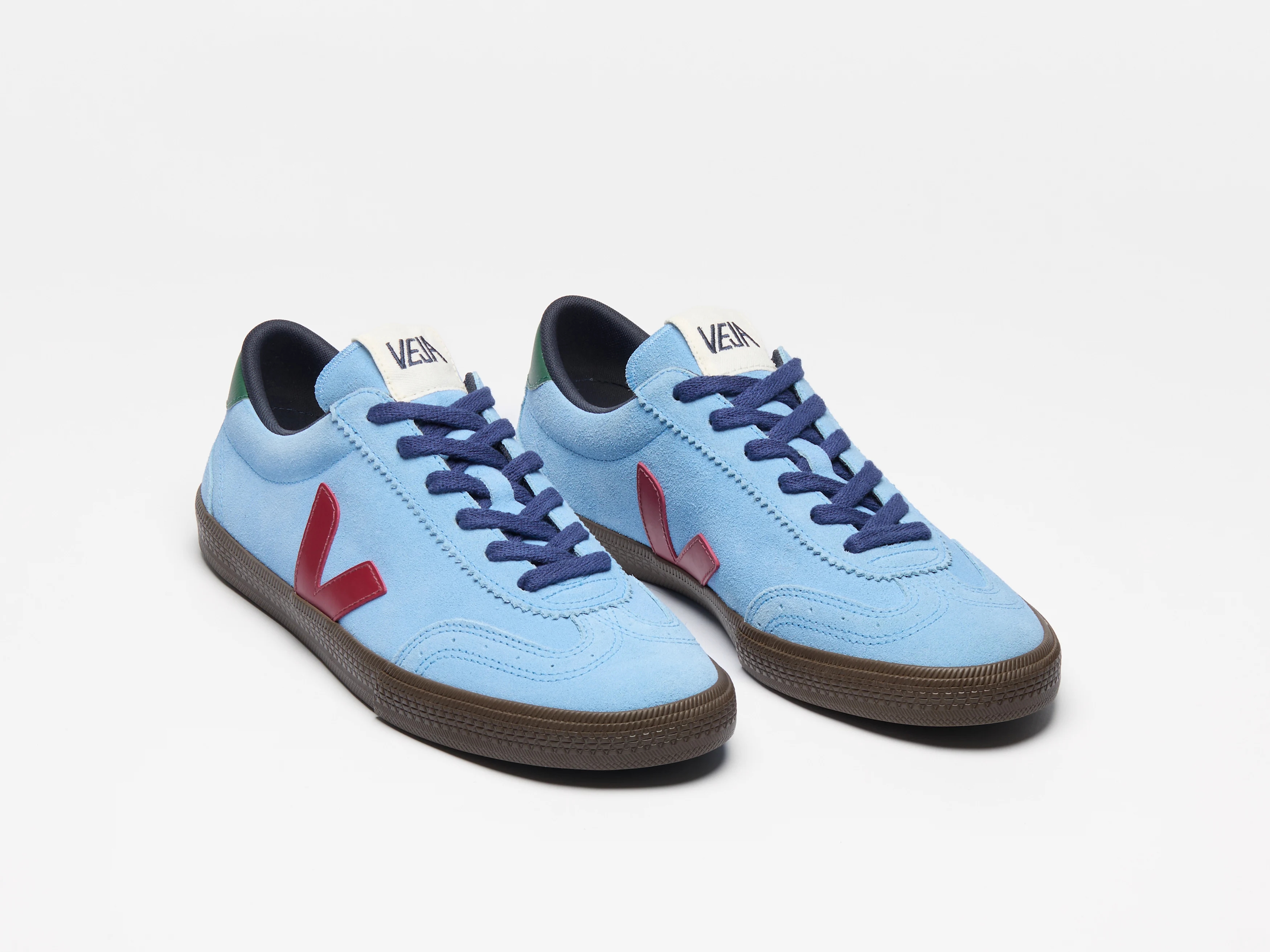 Casual sneakers with blue upper, red side logo, navy laces, and brown soles, placed on a plain background