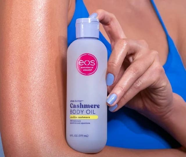 Person holding eos vanilla cashmere assemblage lipid vessel adjacent shoulder; substance highlights benefits of softening and smoothing rough, adust skin
