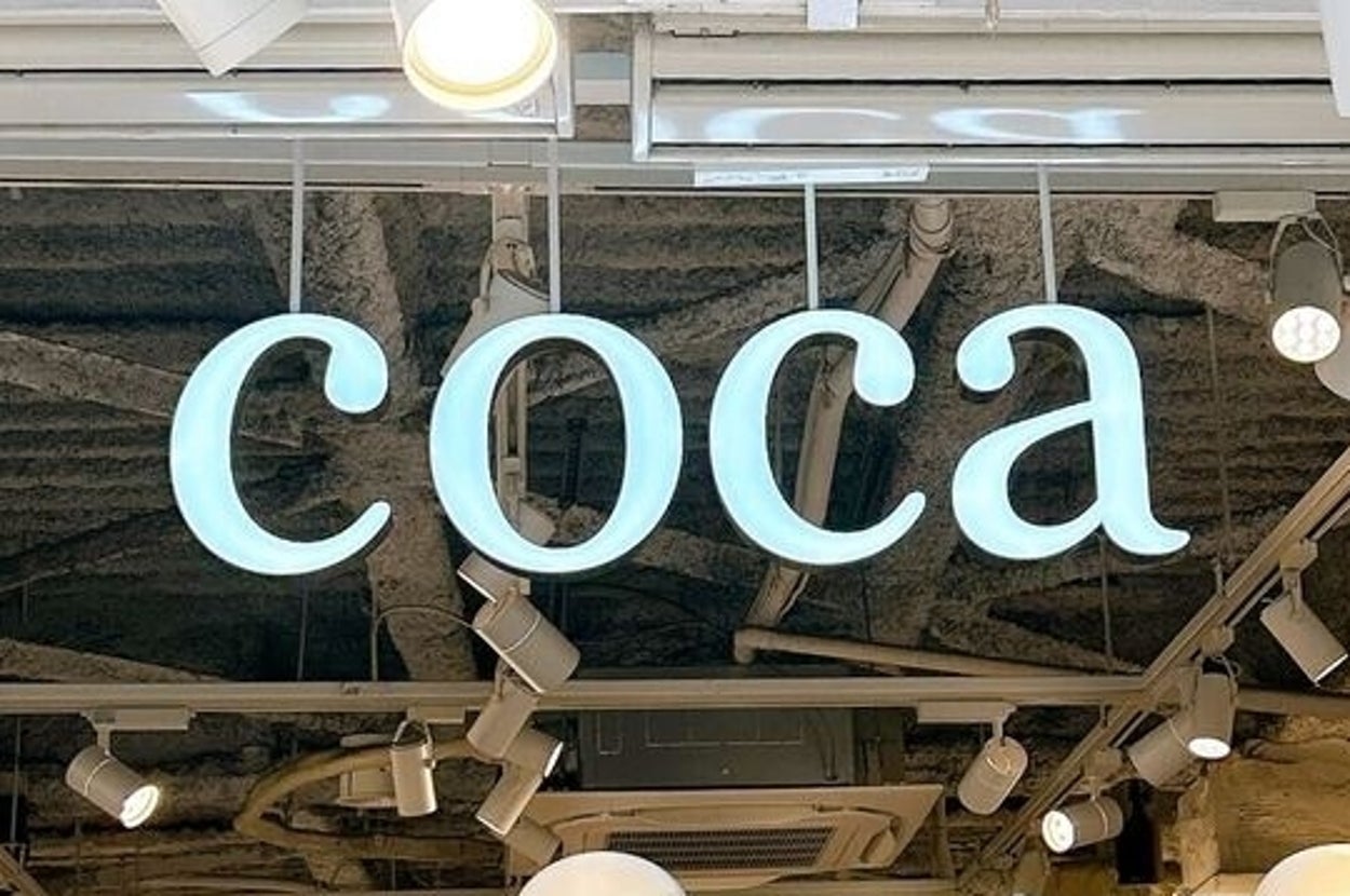 店内に「coca」の青いネオンサインと複数の白いマネキンが配置されています。