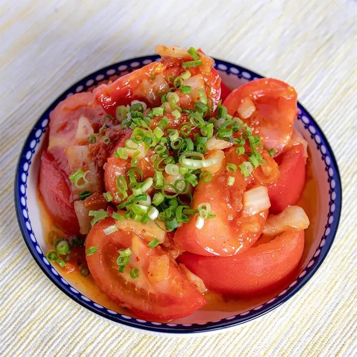 皿に盛られたトマトサラダ。細かく刻んだネギとドレッシングがかかっている。