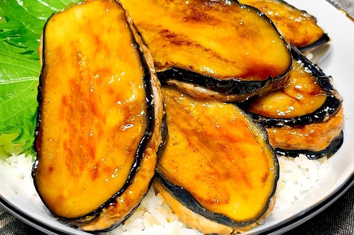 焼きなすのスライスがご飯の上に盛られた料理。葉が添えられている。