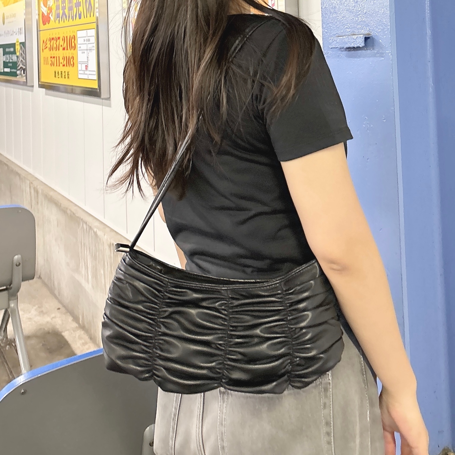 女性が黒いプルドシェイプのバッグを肩にかけて横を向いて立っている。