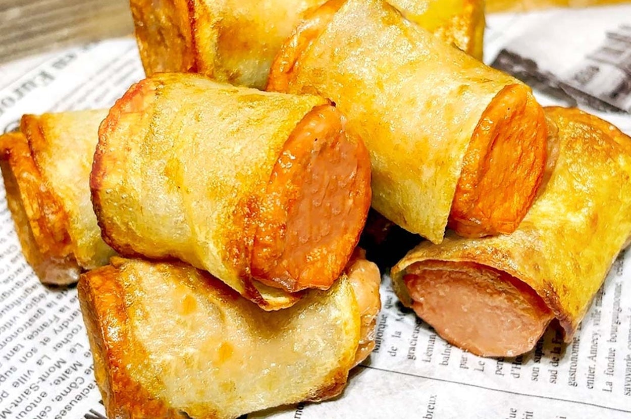 サクッとした生地でソーセージが包まれたスナックが新聞紙の上に盛り付けられています。