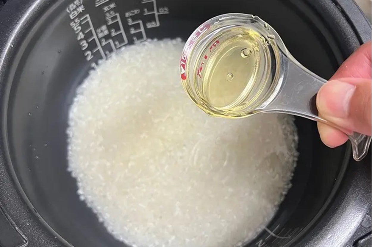 炊飯器に入ったお米に透明な液体を注いでいる手元の画像。