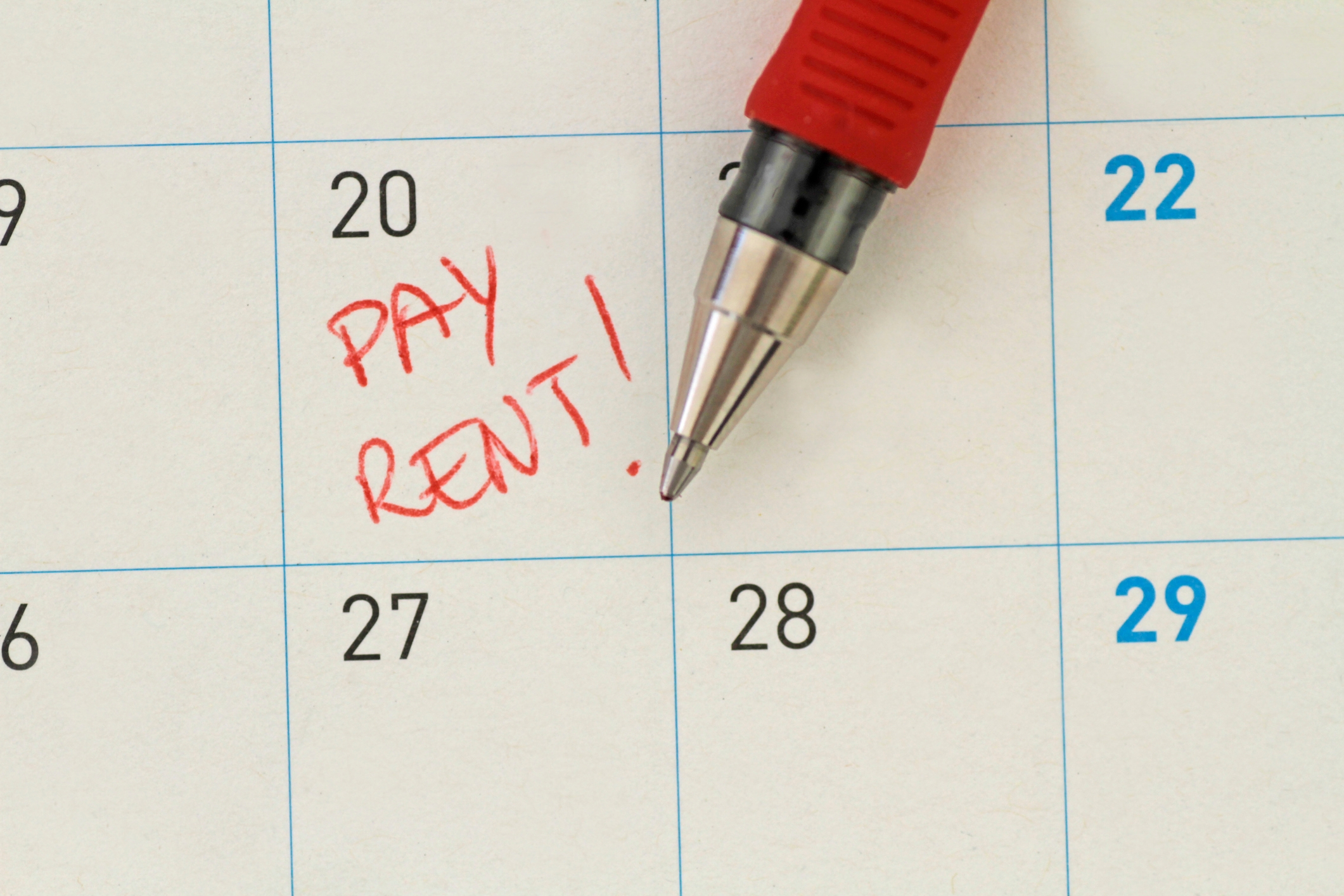 Calendar close-up with a red pen marking "PAY RENT!" on the 28th