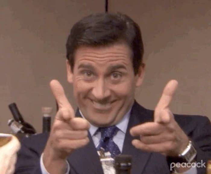 Person in a suit smiles and points fingers in a playful gesture. Office setting