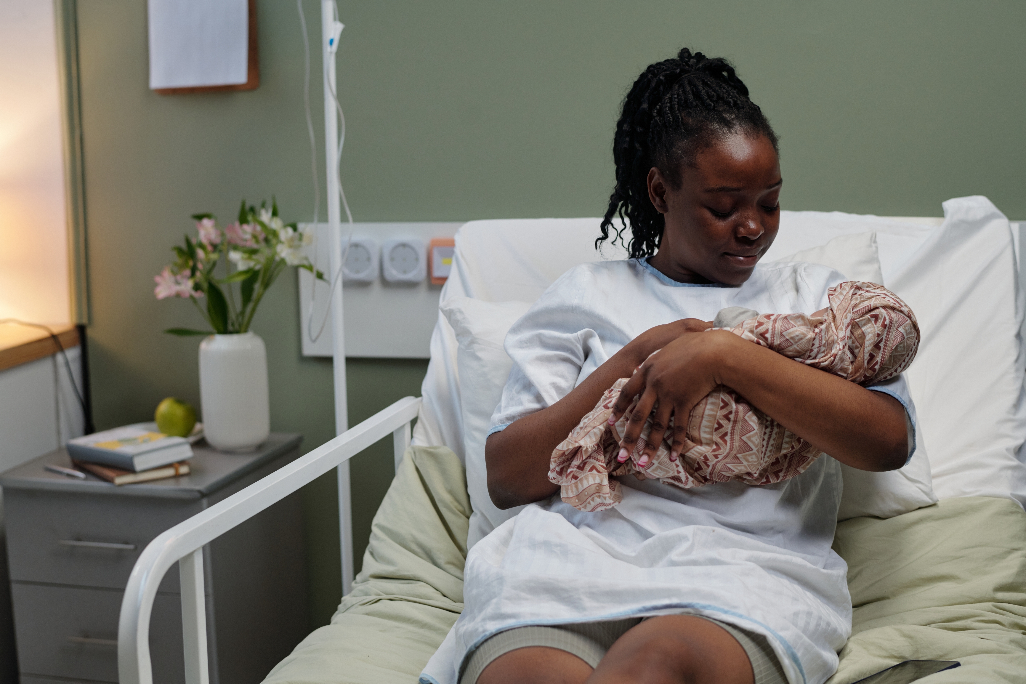 New mother sits in a hospital bed, gently holding and gazing at her newborn wrapped in a blanket