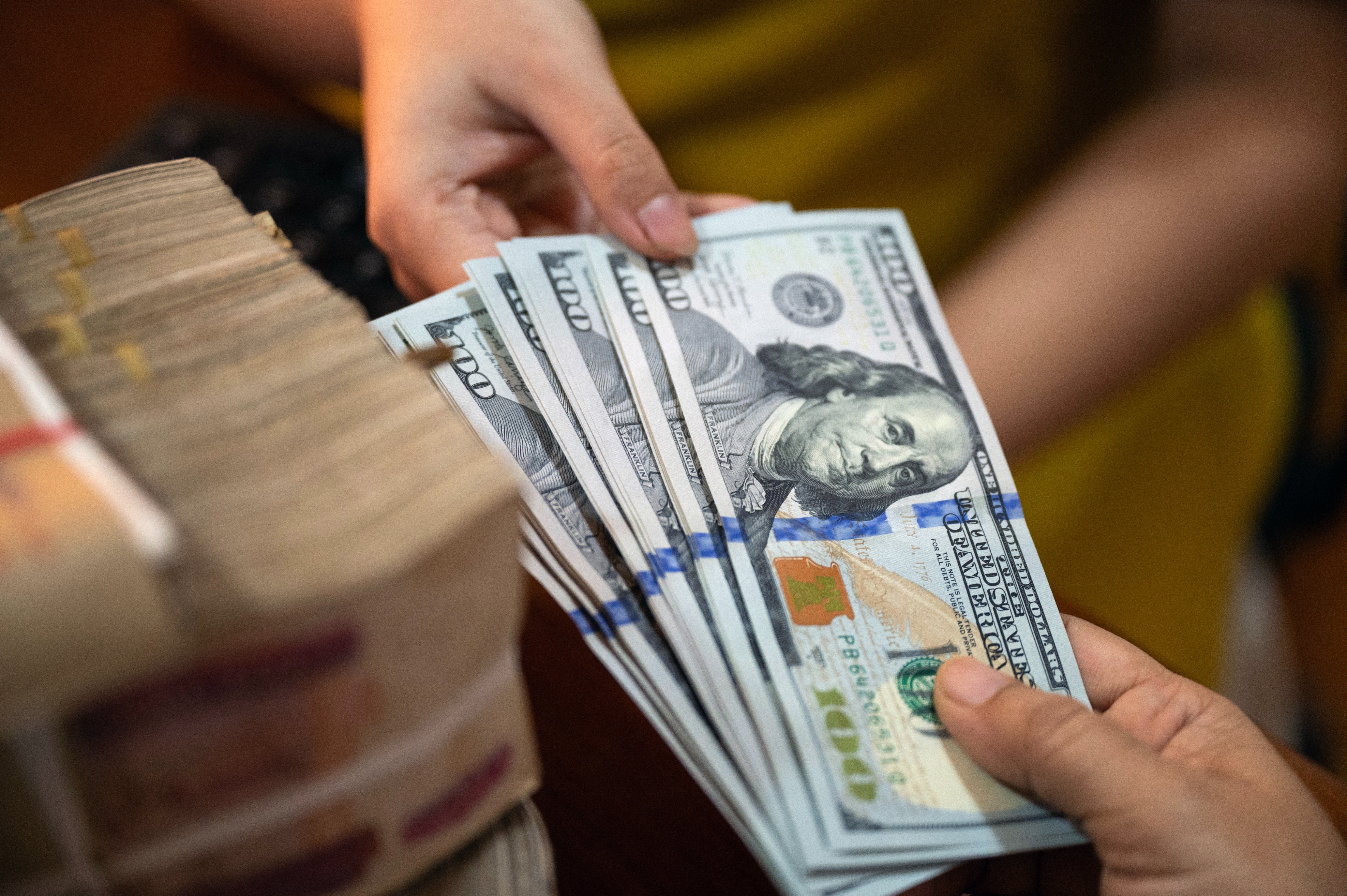Hands exchanging a stack of U.S. hundred-dollar bills, indicating a financial transaction