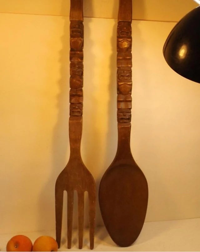 Large decorative woody  fork and spoon with carved handles displayed connected  a partition  adjacent  to a lamp and 2  small