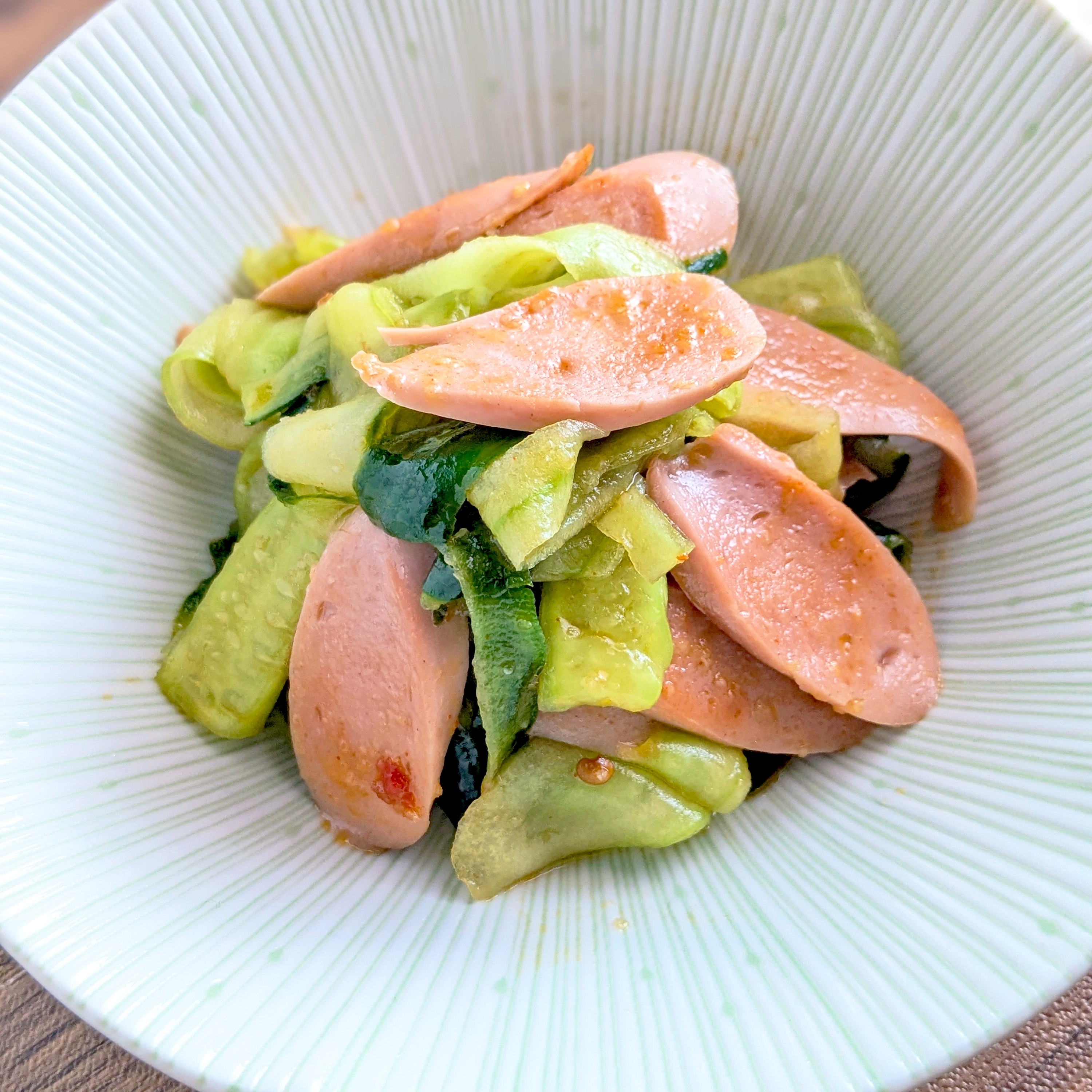 薄切りのソーセージときゅうりが白い器に盛られたサラダ。