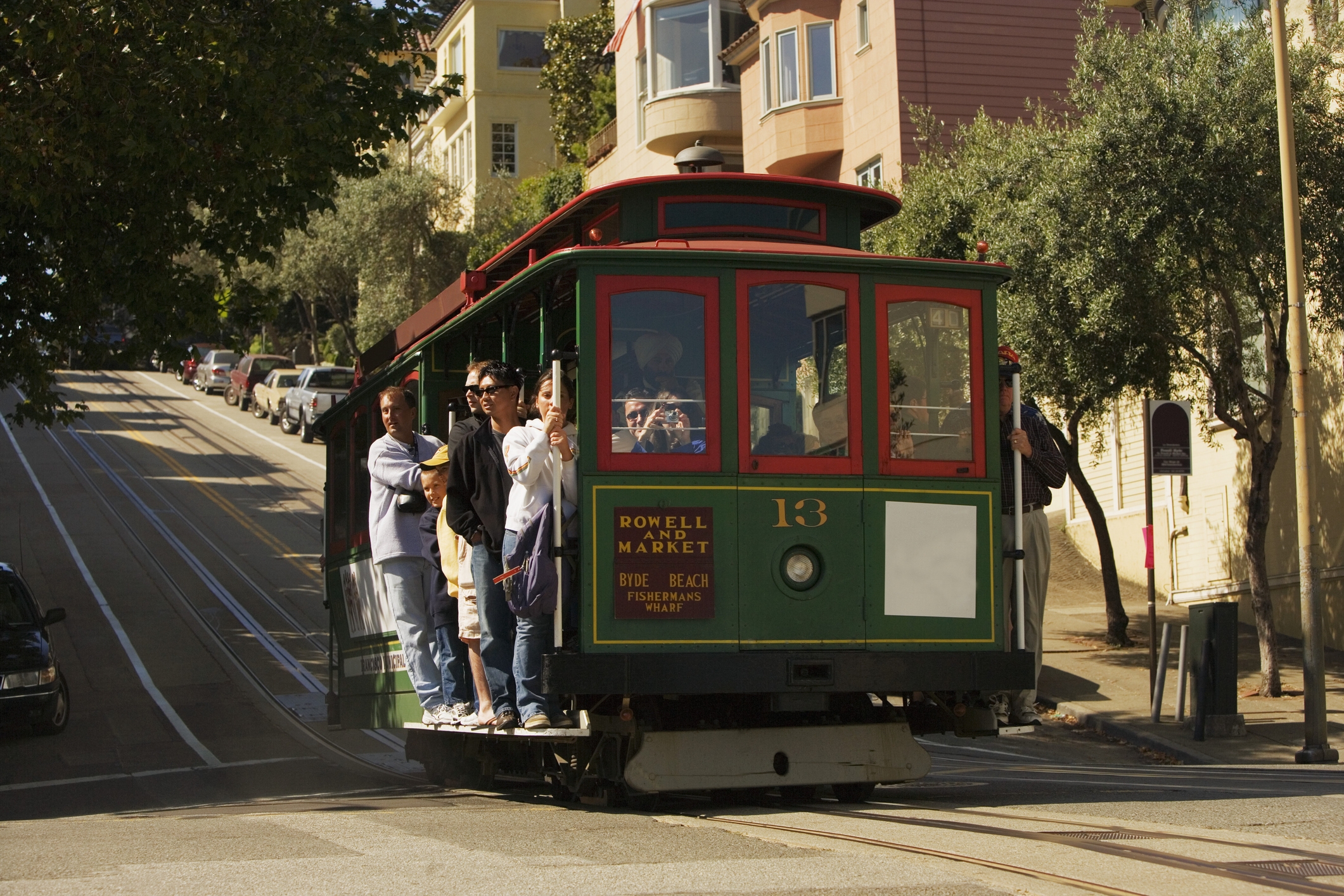 People ride a classic San Francisco cable car up a hilly street, capturing the iconic transport and urban scenery