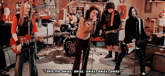 Band performing energetically in a garage with instruments; lead singer at the center. Subtitled lyrics: "Take me away, away, away, away!"