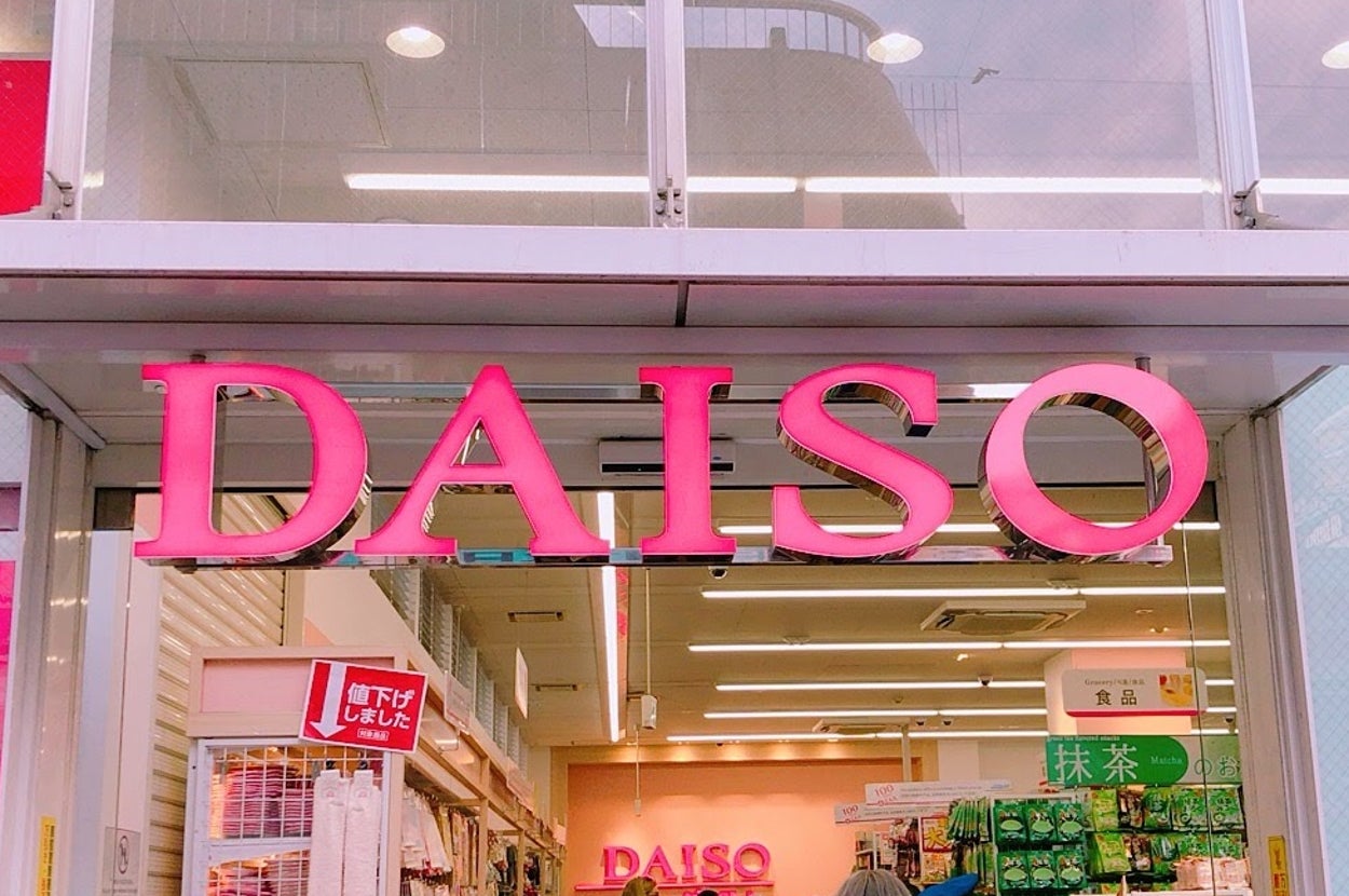 ダイソーの店舗入口。多くの人々が店内に出入りしている。店周りには様々な商品が並んでいる。