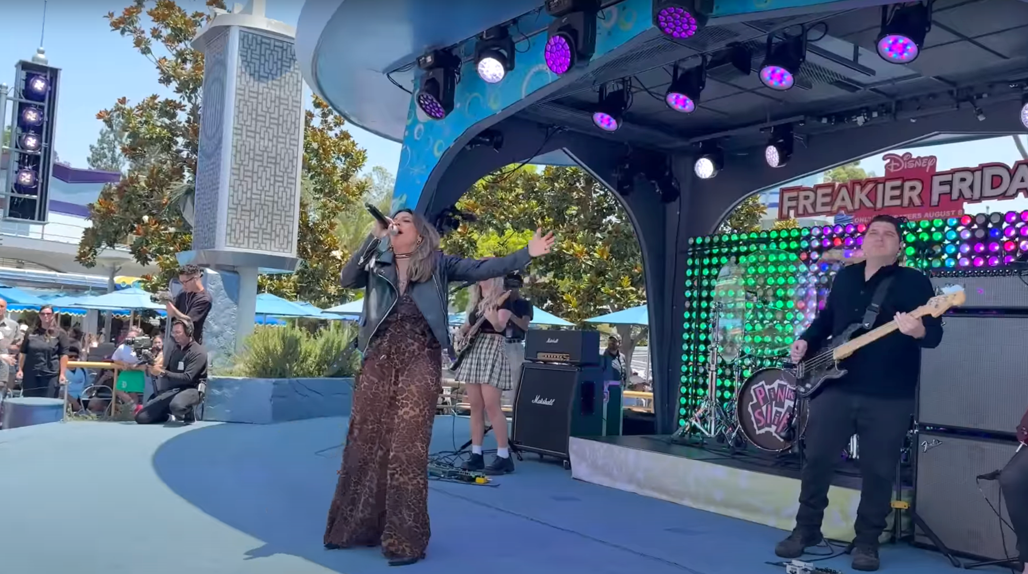 A singer performs energetically on an outdoor stage with a band at a Disney event