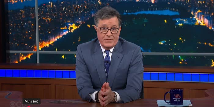 Stephen Colbert sits at a desk on set of The Late Show