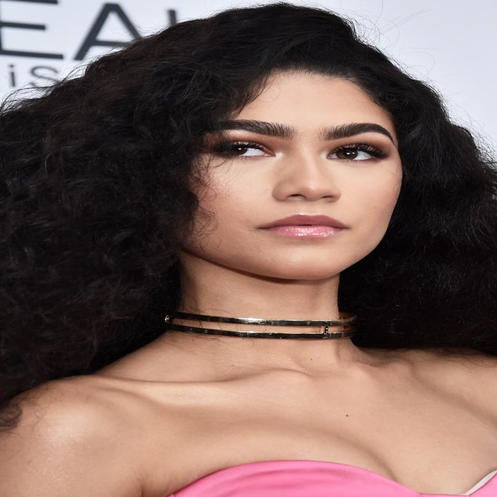 A person with voluminous, wavy hair on a red carpet wears a strapless, elegant outfit and a double choker necklace