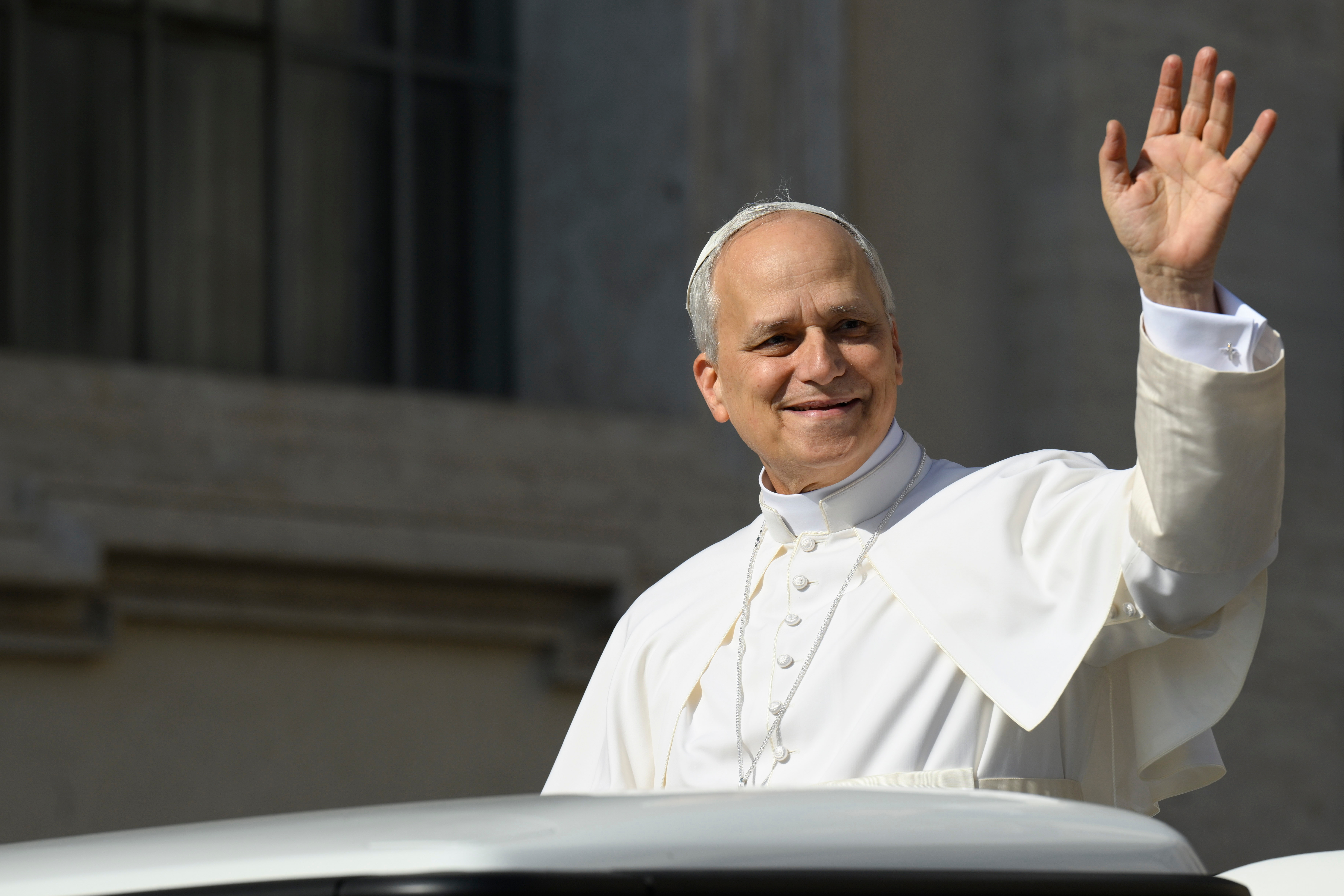 A man in clerical attire waves while standing, appearing to greet a crowd