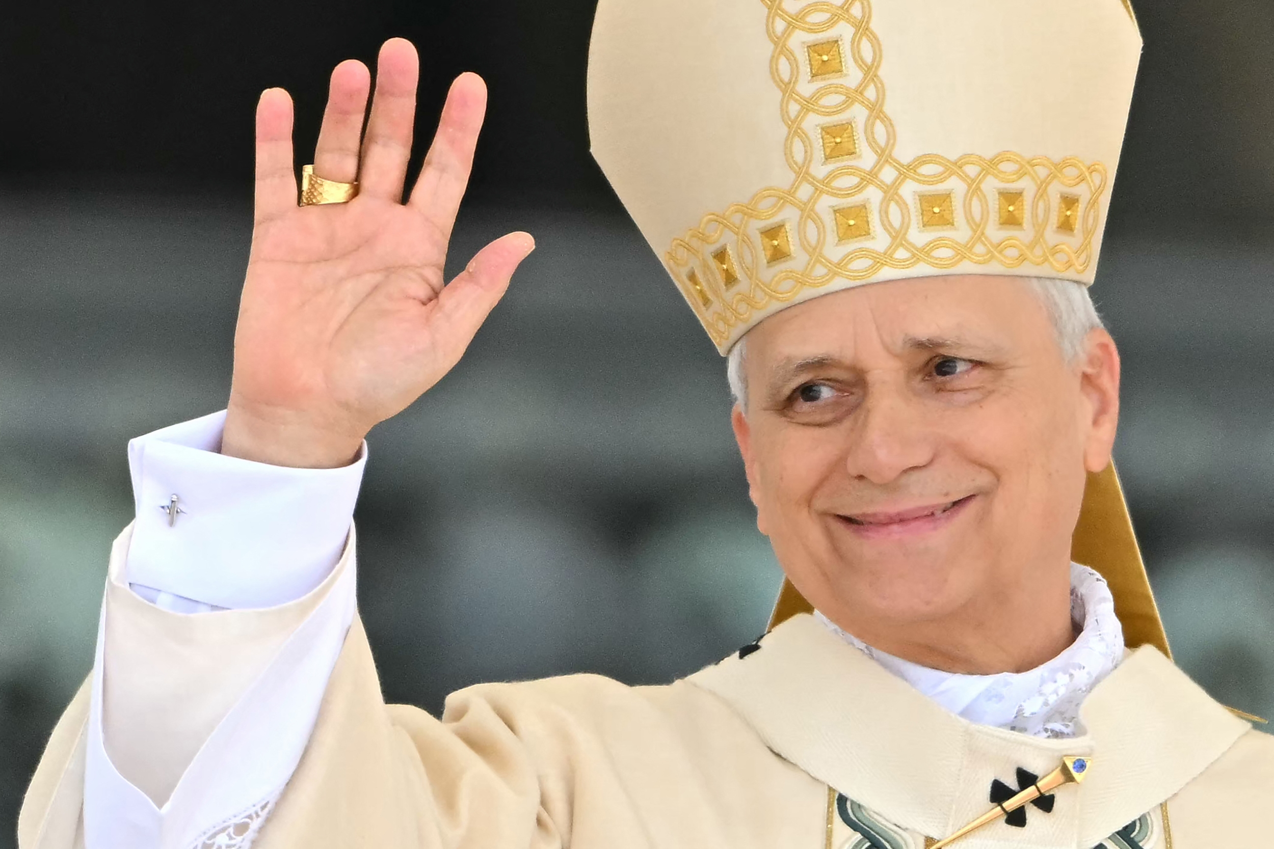A religious leader in ceremonial attire waves, wearing an ornate hat and robe