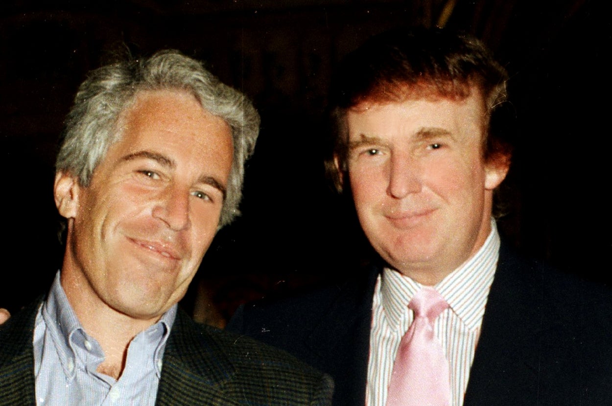 Two men at an event; one in a blazer and jeans, the other in a suit with a pink tie