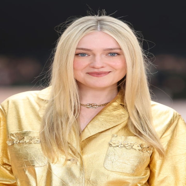 A person in a stylish, gold silk shirt poses on the red carpet, smiling