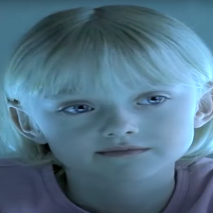 A young child with short blonde hair looks thoughtfully at an adult off-camera